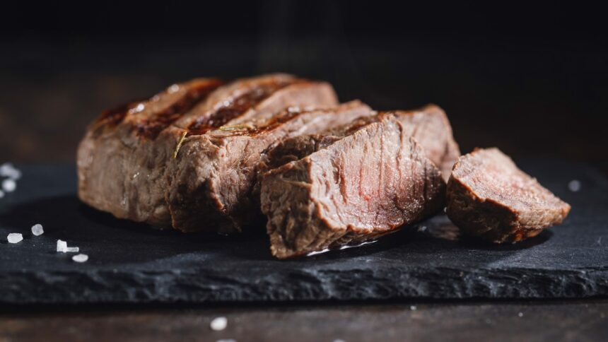 Baby beef grelhado e fatiado em tábua escura, com sal grosso e ramo de alecrim.