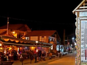 Rua noturna iluminada em Monte Verde com termômetro decorado e pessoas em bar.