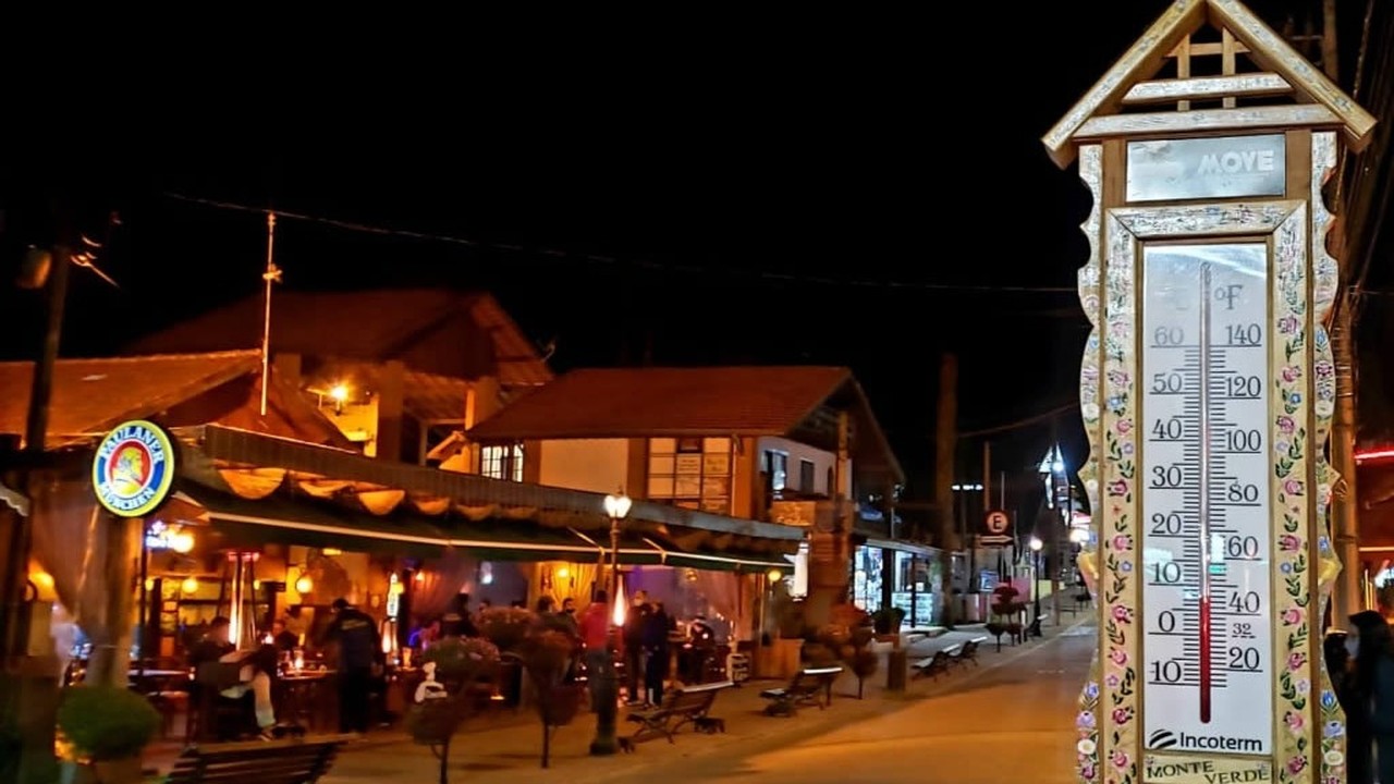 Rua noturna iluminada em Monte Verde com termômetro decorado e pessoas em bar.