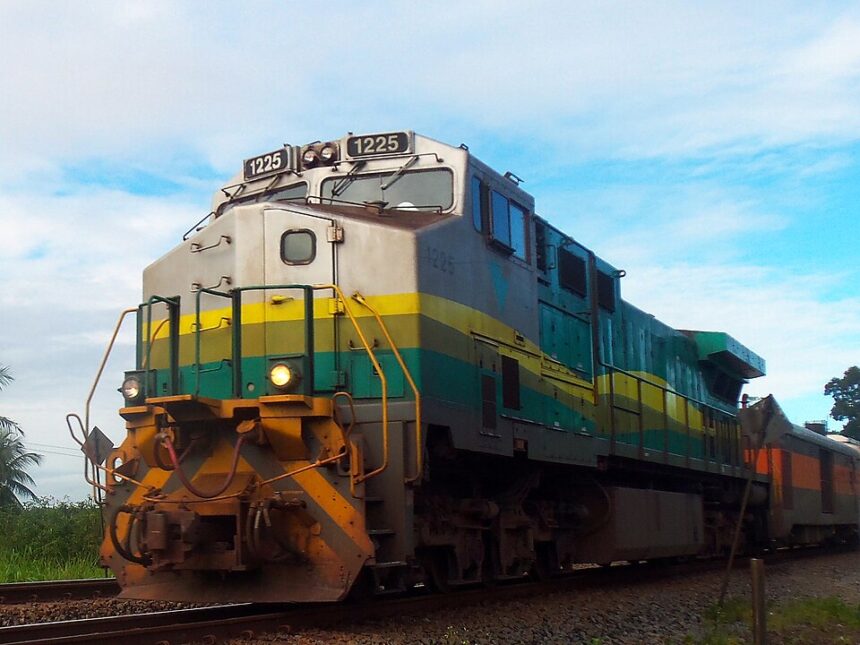 Locomotiva 1225 em tons de verde, amarelo e cinza em trilhos, com faróis acesos.