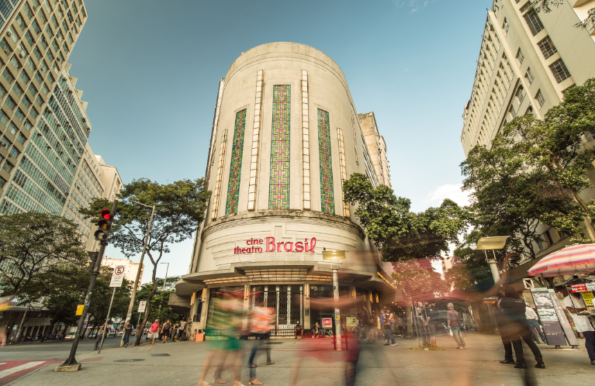 Fachada Art Deco do Cine Theatro Brasil com letreiro vermelho e pedestres borrados na rua