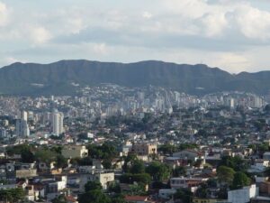 Vista aérea panorâmica de Belo Horizonte com muitos edifícios e montanhas ao fundo.