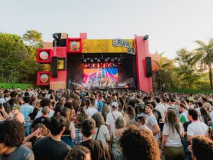 Multidão no Festival Sarará, palco com telão mostrando artista, luzes e logos Amstel.