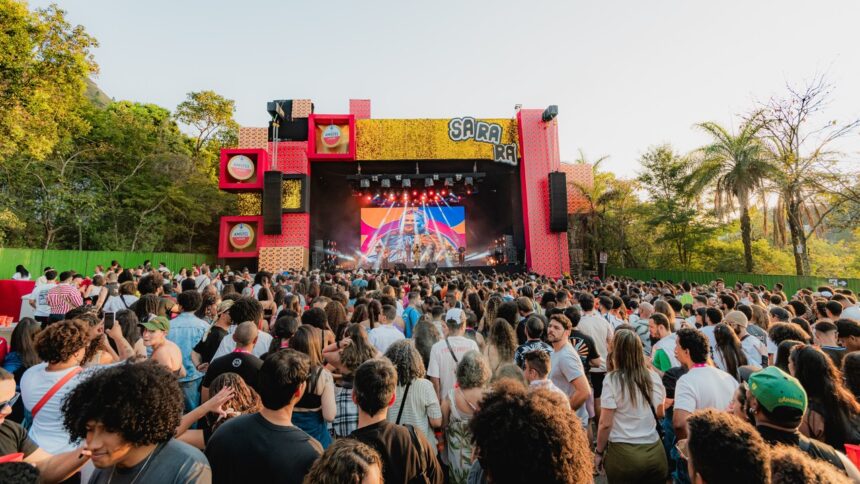 Multidão no Festival Sarará, palco com telão mostrando artista, luzes e logos Amstel.