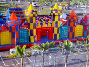 Brinquedo inflável gigante, colorido, em forma de castelo, com torres e obstáculos, em estacionamento.