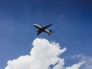 Avião branco de passageiros voando em céu azul claro com nuvens no canto inferior