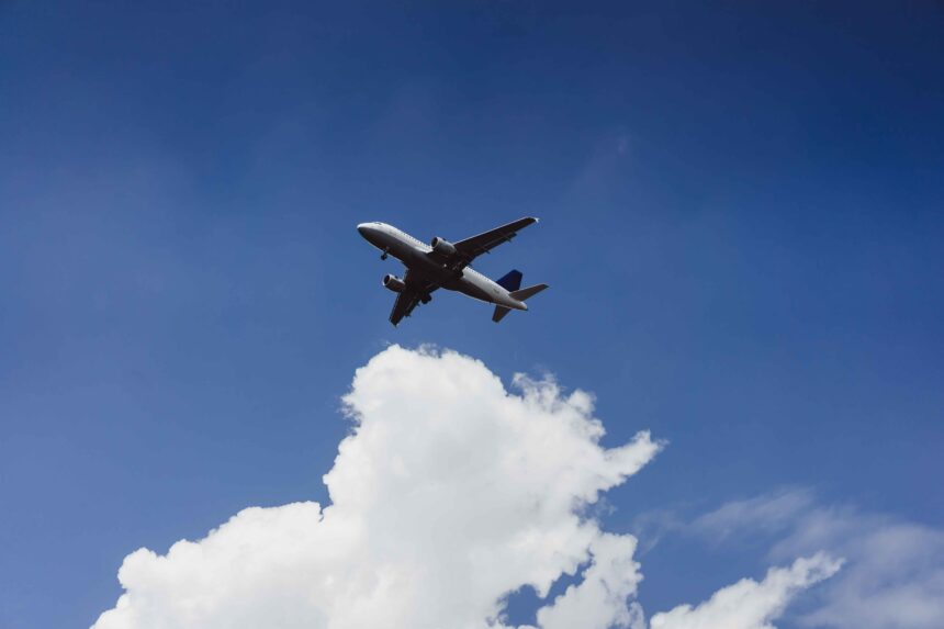 Avião branco de passageiros voando em céu azul claro com nuvens no canto inferior