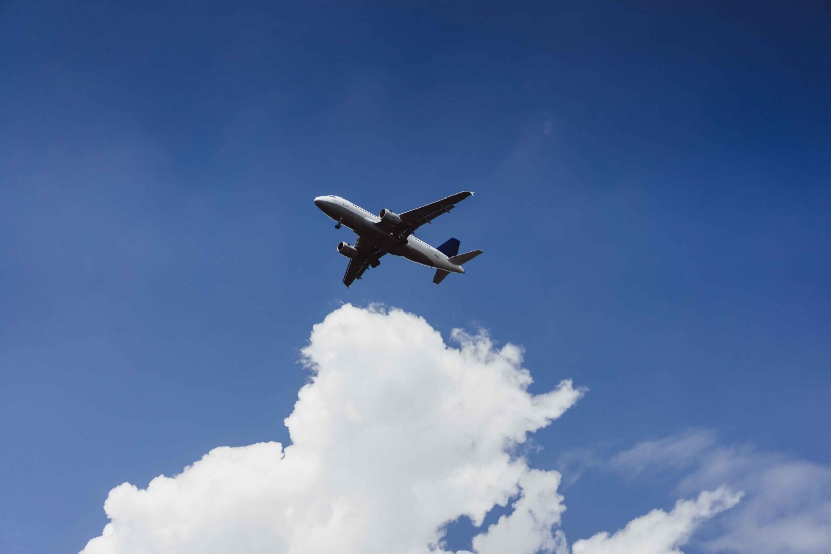 Avião branco de passageiros voando em céu azul claro com nuvens no canto inferior