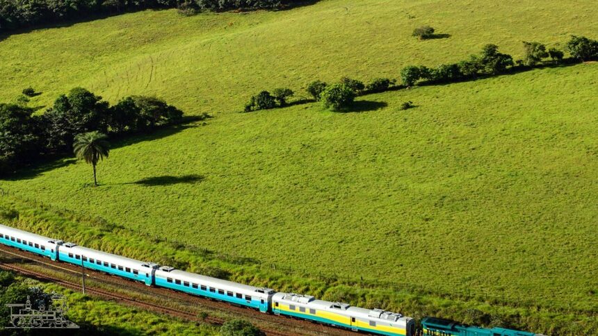 Trem de passageiros multicolorido em trilhos através de um vasto campo verde com árvores e colinas.