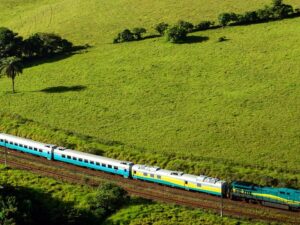 Trem de passageiros longo em trilhos através de paisagem verde e montanhosa, com logotipo Vale.