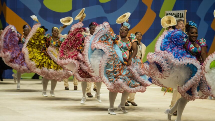 Dançarinas e dançarinos em trajes juninos coloridos e chapéus de palha dançando alegremente.