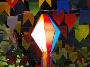Bandeirinhas coloridas e uma lanterna iluminada decoram festa junina à noite.