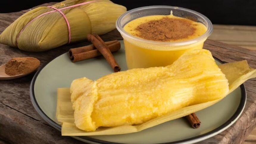 Pamonha, curau com canela, canela em pó e paus em prato verde sobre madeira.