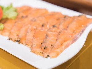 Fatias finas de salmão curado com endro em um prato branco, guarnecido com alface.
