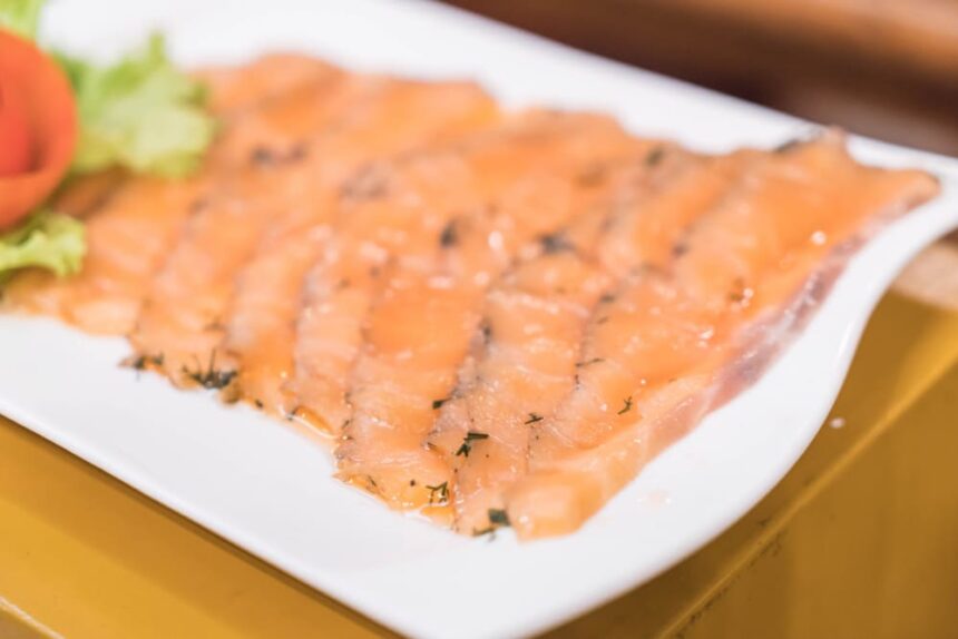 Fatias finas de salmão curado com endro em um prato branco, guarnecido com alface.
