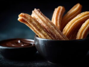 Churros açucarados em tigela preta, com molho de chocolate em outra tigela escura.