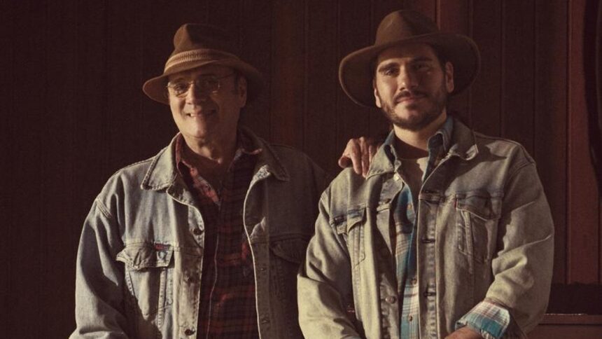 Dois homens de chapéu e jaqueta jeans sorriem, um com o braço no ombro do outro.