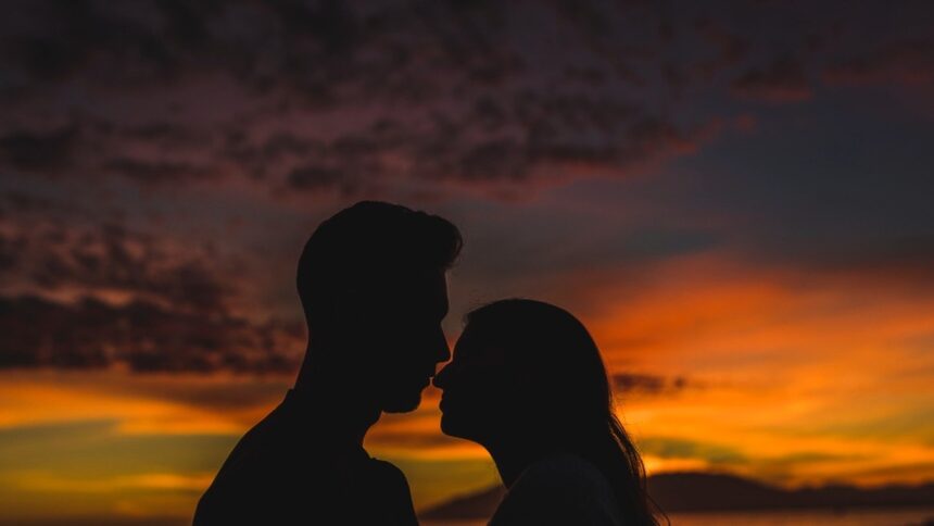 Silhuetas de um casal se tocando o nariz em um pôr do sol colorido.
