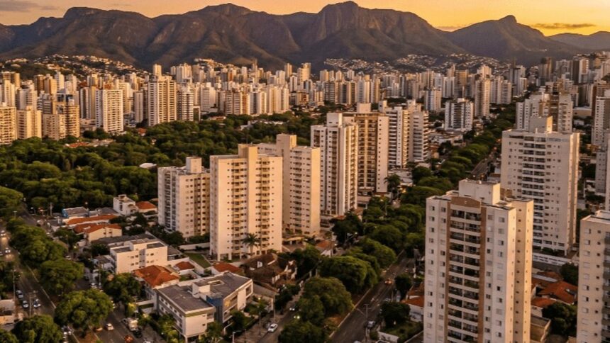 Vista aérea da cidade com prédios, áreas verdes e montanhas ao fundo no entardecer