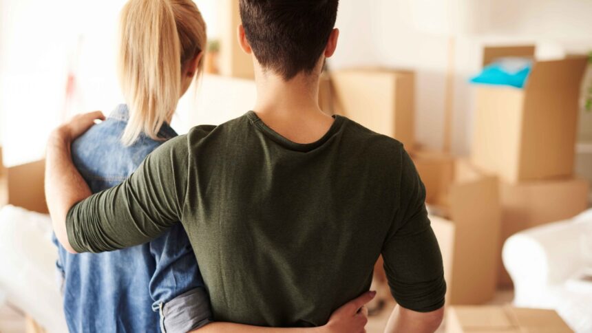 Casal de costas, abraçado, olhando caixas de mudança em um cômodo de casa nova