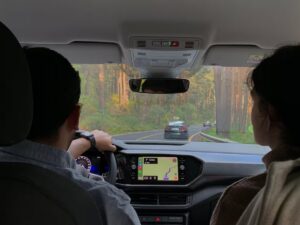Pessoas dentro de um carro, dirigindo em estrada arborizada com GPS ativo no painel