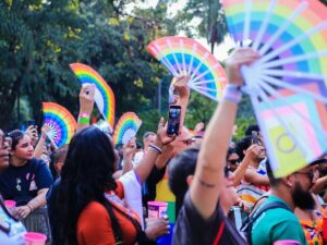 Uma multidão de pessoas com leques arco-íris e celulares em um evento ao ar livre