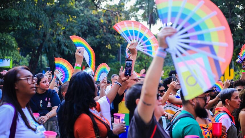 Uma multidão de pessoas com leques arco-íris e celulares em um evento ao ar livre