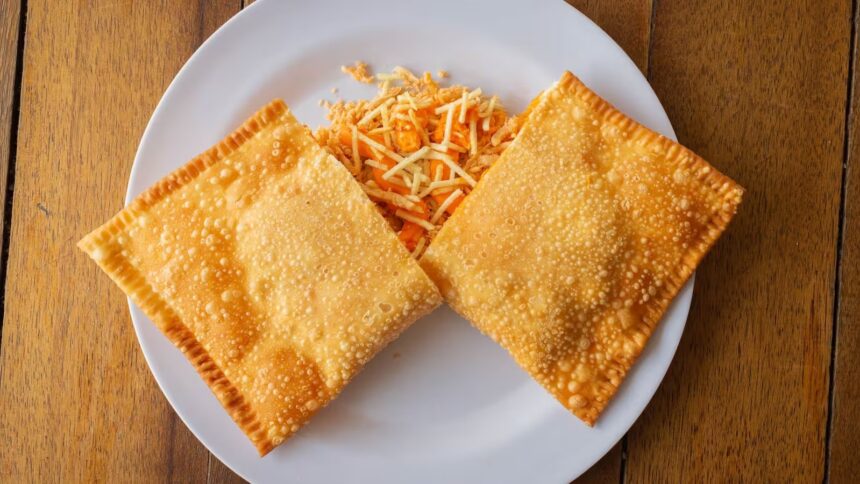 Dois pastéis fritos dourados em prato branco com recheio e batata palha