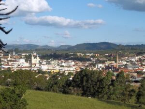 Vista elevada de São Gonçalo do Sapucaí, com edifícios, igrejas, chaminé industrial e morros