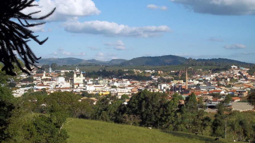 Vista elevada de São Gonçalo do Sapucaí, com edifícios, igrejas, chaminé industrial e morros