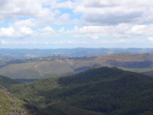 Paisagem montanhosa com vales verdes, rochas, cidade distante e céu azul com nuvens