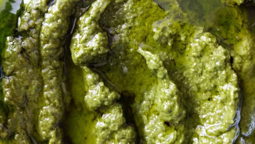 Close-up superior de molho pesto verde vibrante com textura pastosa e reflexos de azeite