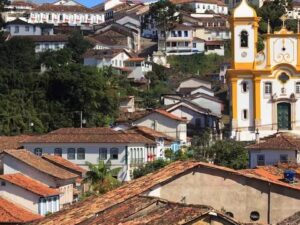 Cidade histórica de Minas Gerais com casas de telhados de barro e igreja barroca amarela em colina.