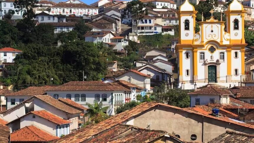 Cidade histórica de Minas Gerais com casas de telhados de barro e igreja barroca amarela em colina.