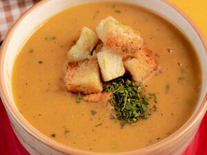 Close-up de caldo cremoso em tigela com croutons crocantes e ervas verdes frescas