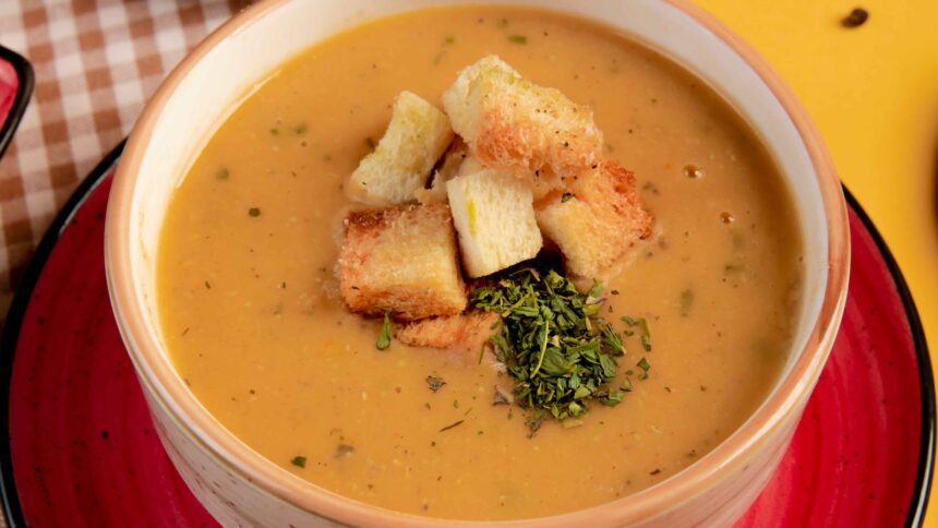 Close-up de caldo cremoso em tigela com croutons crocantes e ervas verdes frescas