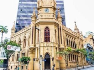 Edifício histórico do Museu de Artes e Ofícios em BH com torre do relógio e arranha-céu.