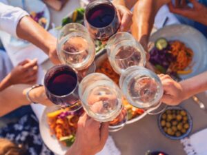 Mãos de várias pessoas brindando com taças de vinho tinto e branco em uma refeição