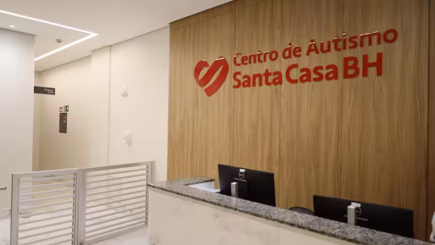Recepção do Centro de Autismo Santa Casa BH com balcão, monitores e sinalização com logo e nome.