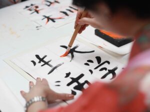 Pessoa escreve ideogramas chineses em papel com pincel e tinta preta e laranja