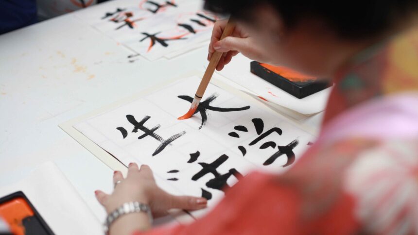 Pessoa escreve ideogramas chineses em papel com pincel e tinta preta e laranja