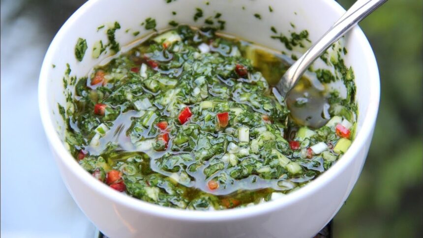 Tigela branca com chimichurri fresco, ervas picadas, pimenta vermelha, óleo e uma colher de metal