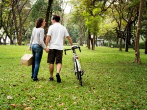 Um casal caminha de mãos dadas em um parque com bicicleta e cesta de piquenique