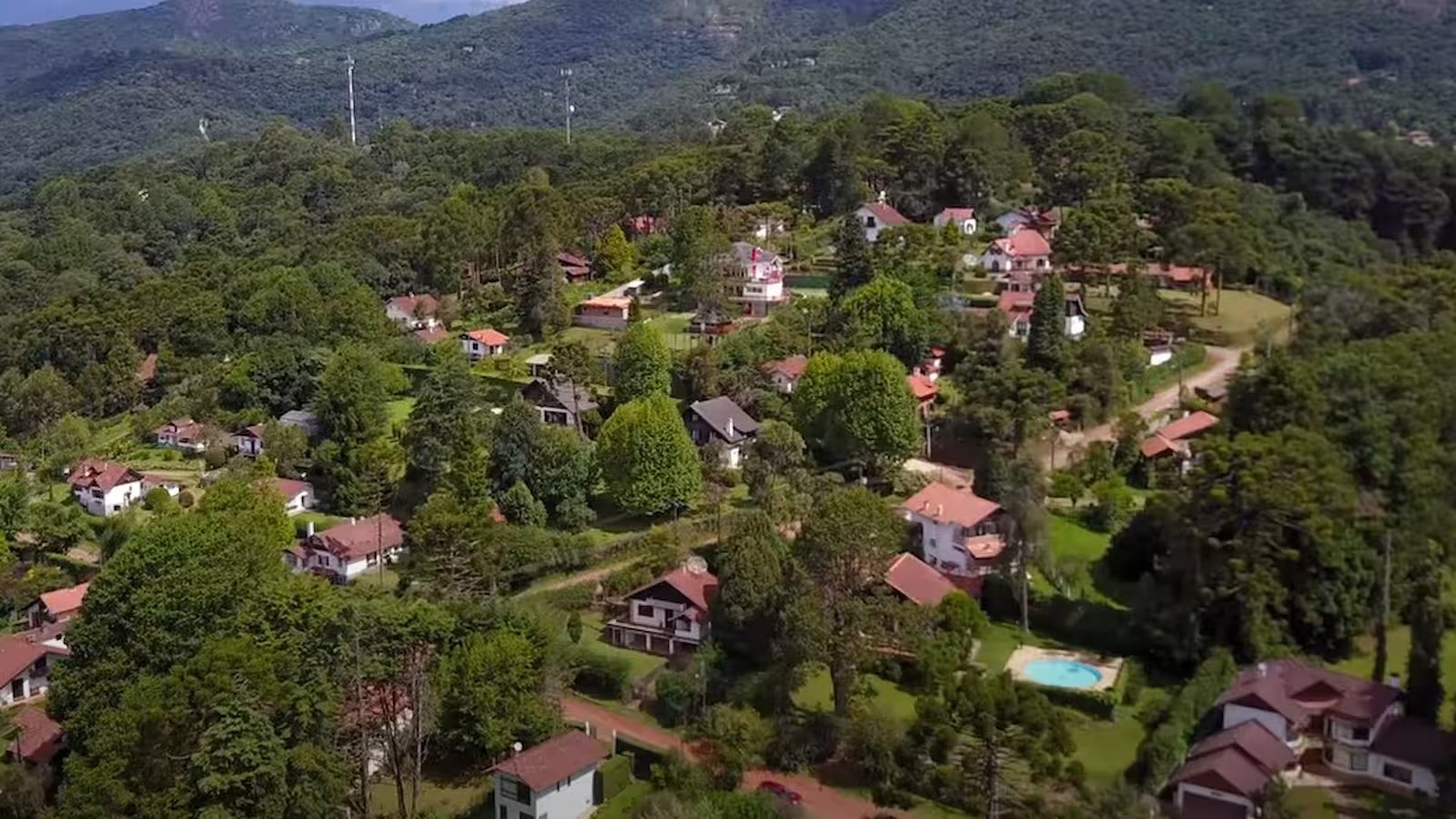 Vista aérea de vilarejo montanhoso com casas telhado vermelho cercadas por árvores densas