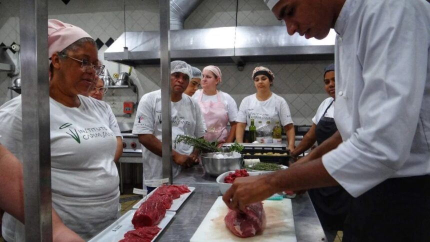 Chef prepara carne em cozinha com alunos do Instituto Capim Santo observando, ingredientes no balcão