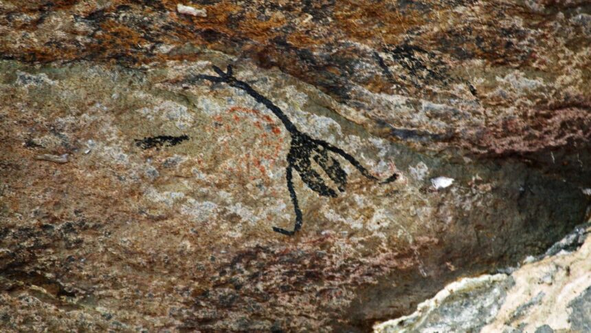 Desenho preto estilizado de figura humana ou animal em parede de rocha com tons marrons e vermelhos