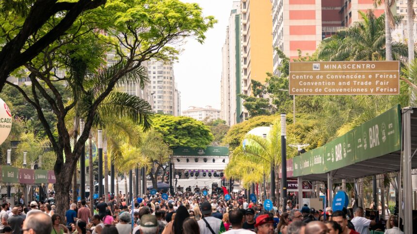 Multidão em festa de rua com árvores, prédios e placas, incluindo "MINASCENTRO"