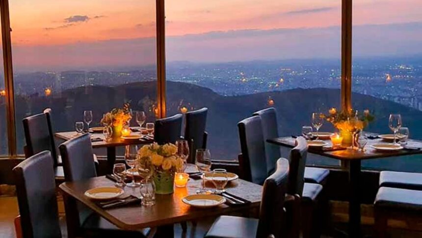 Mesas de restaurante com vista panorâmica da cidade ao anoitecer, montanhas e luzes
