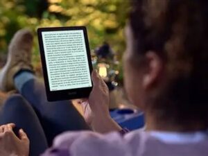 Pessoa lê e-reader preto com texto em tela, sentada ao ar livre, pernas esticadas
