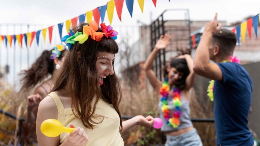 Mulher sorridente com coroa de flores e glitter no rosto, segurando maraca em festa de carnaval